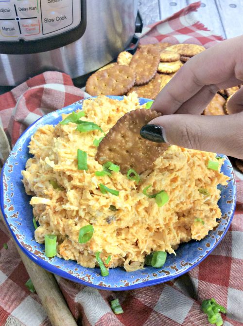 a townhouse cracker being dipped with buffalo chicken dip topped with green onions.