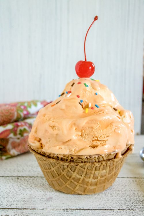 a waffle bowl full of orange creamsicle ice cream topped with sprinkles and a cherry.
