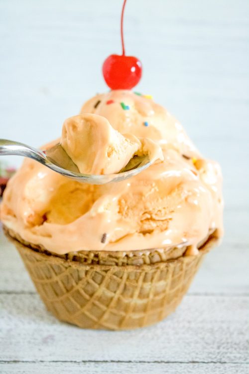 a spoon lifting out a bite or orange creamsicle ice cream from a waffle cone bowl.