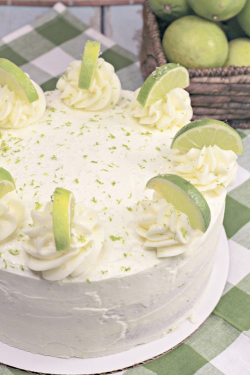 a margarita cake garnished with lime slices and lime zest on a green tablecloth.