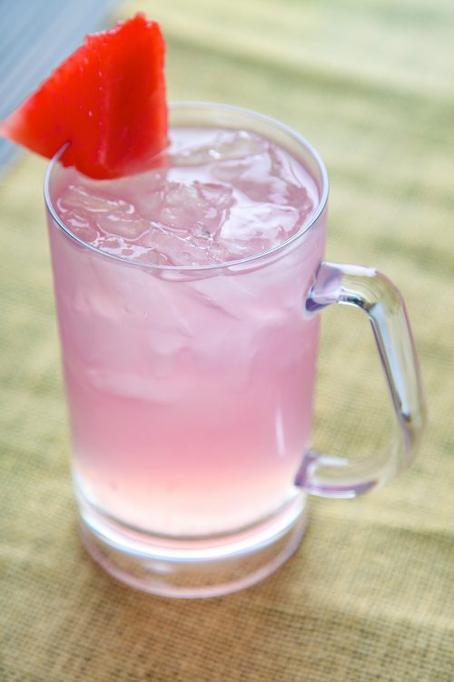a glass mug of pink hippie juice garnished with a wedge of watermelon.