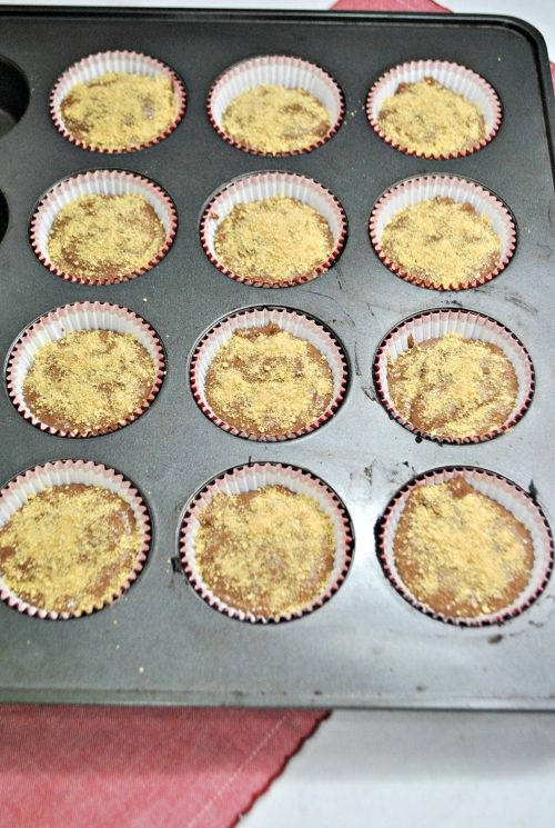 12 cupcake liners filled with chocolate batter and graham cracker crumbs.