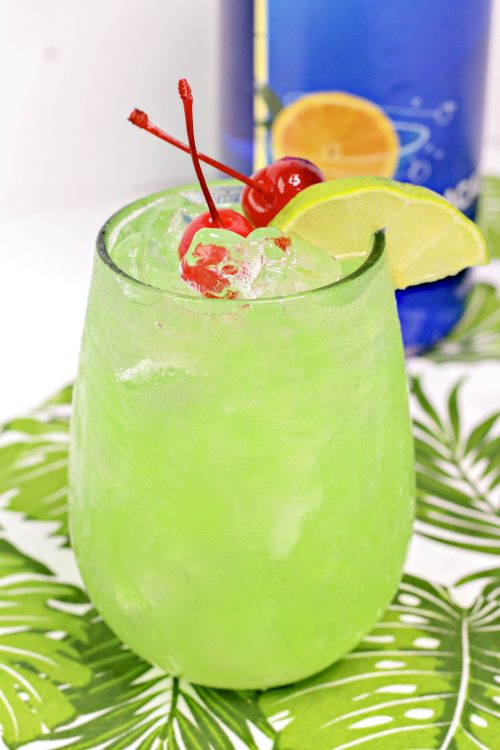 a bright green mermaid cocktail garnished with marachino cherries and lime.