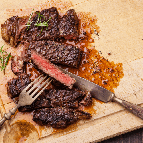 a steak slicing into a ribeye steak on a wooden cutting board.
