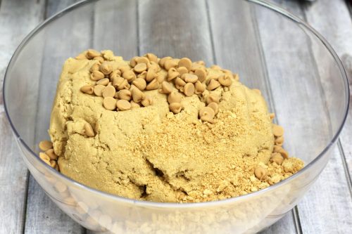 a clear mixing bowl with peanut butter cookie dough, peanut butter chips, and crushed nutter butters.