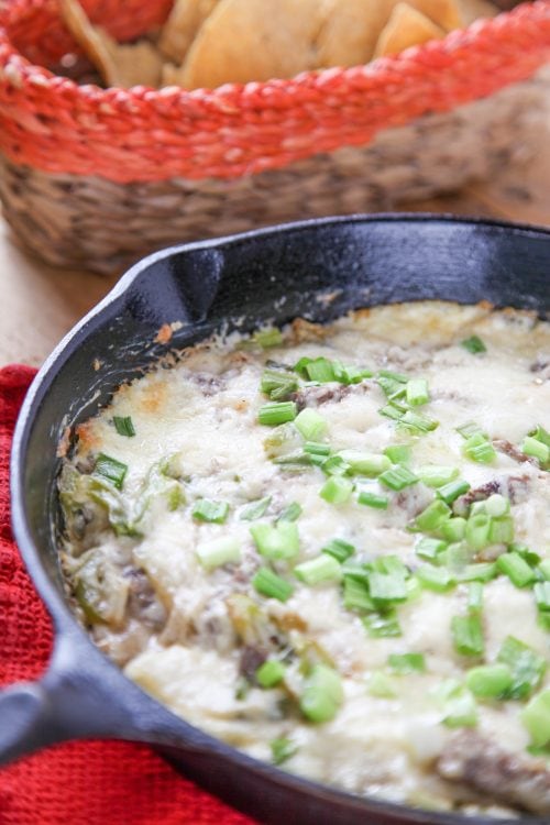 philly cheesesteak dip garnished with green onions in a cast iron skillet.