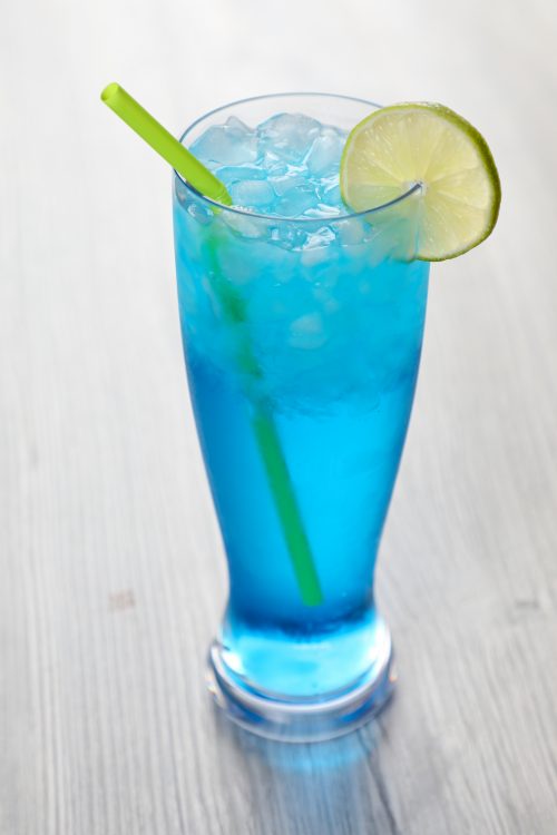 a blue sex in the driveway cocktail in a tall glass with a green straw and a lime wheel