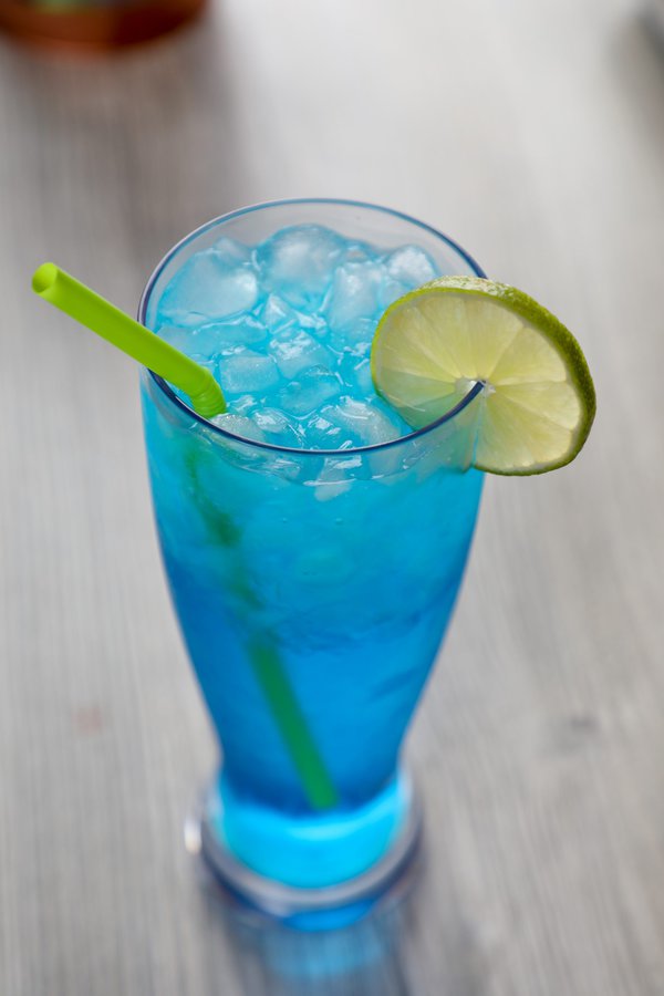 a blue cocktail garnished with ice and a lime wheel.