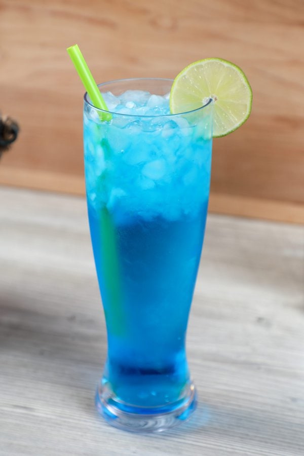 a blue vodka cocktail cocktail on a wooden background garnished with a lime wheel.