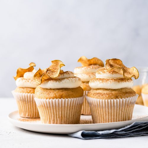 cupcakes with cinnamon buttercream topped with a dried apple chip on a white plate.