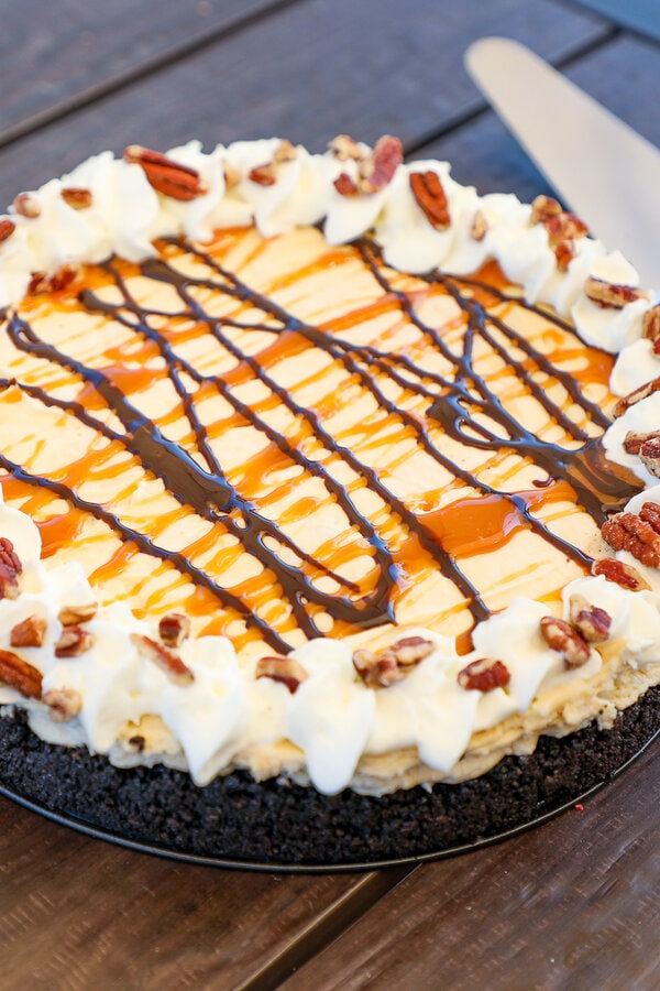 a caramel pie with an oreo crust garnished with cool whip and chopped pecans.