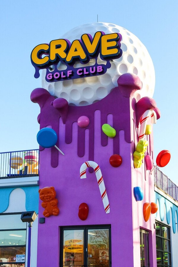 the entrance to crave mini gold which is a purple building with candy and a gummy bear.