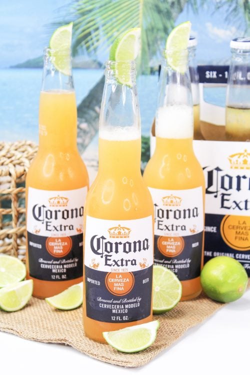 three corona sunrise cocktails in beer bottles garnished with lime.