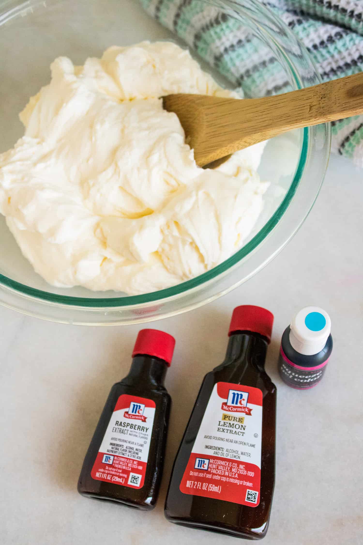 a bowl with no churn ice cream with bottles of raspberry extract, lemon extract, and blue gel food coloring.