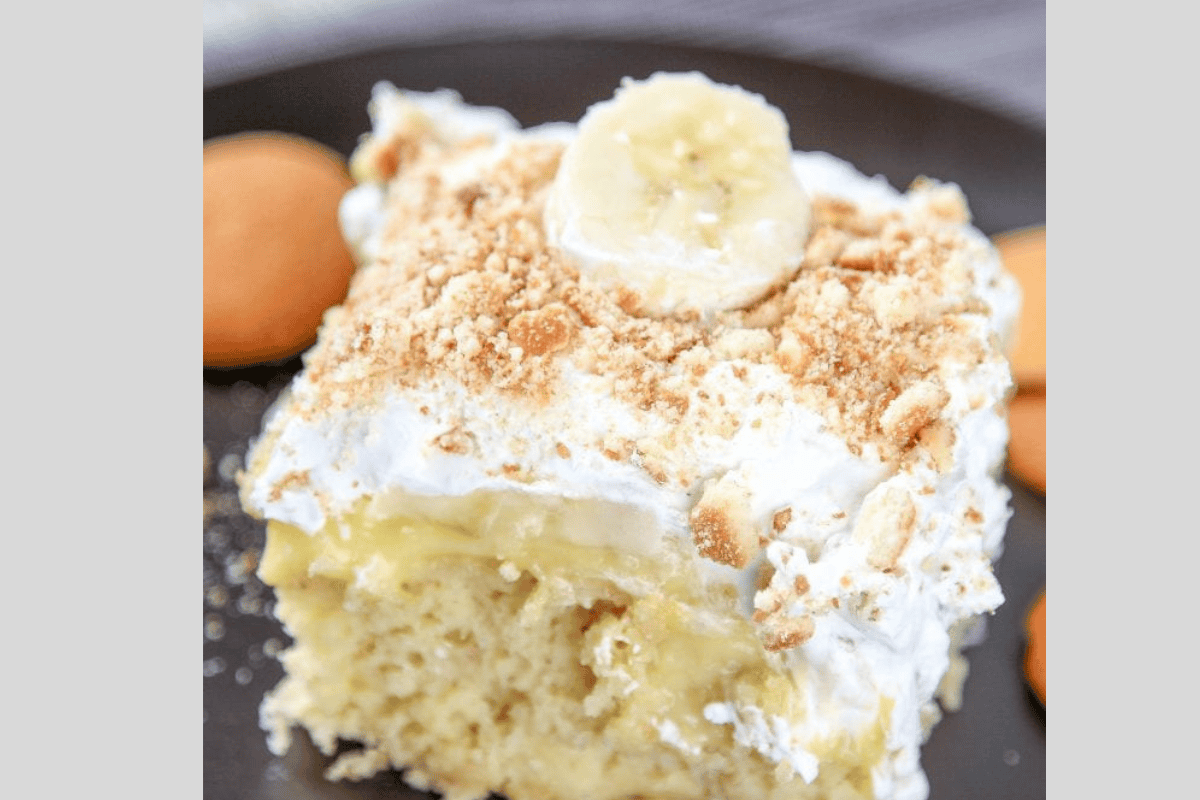 A slice of banana pudding cake topped with sliced bananas and crushed vanilla wafers.