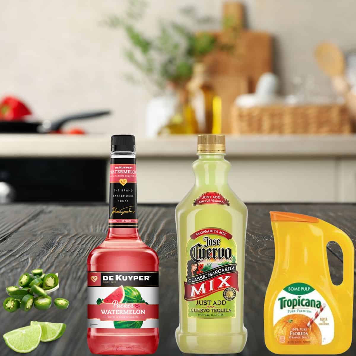 limes, jalapenos, watermelon liquor, margarita mix, and orange juice on a counter. 