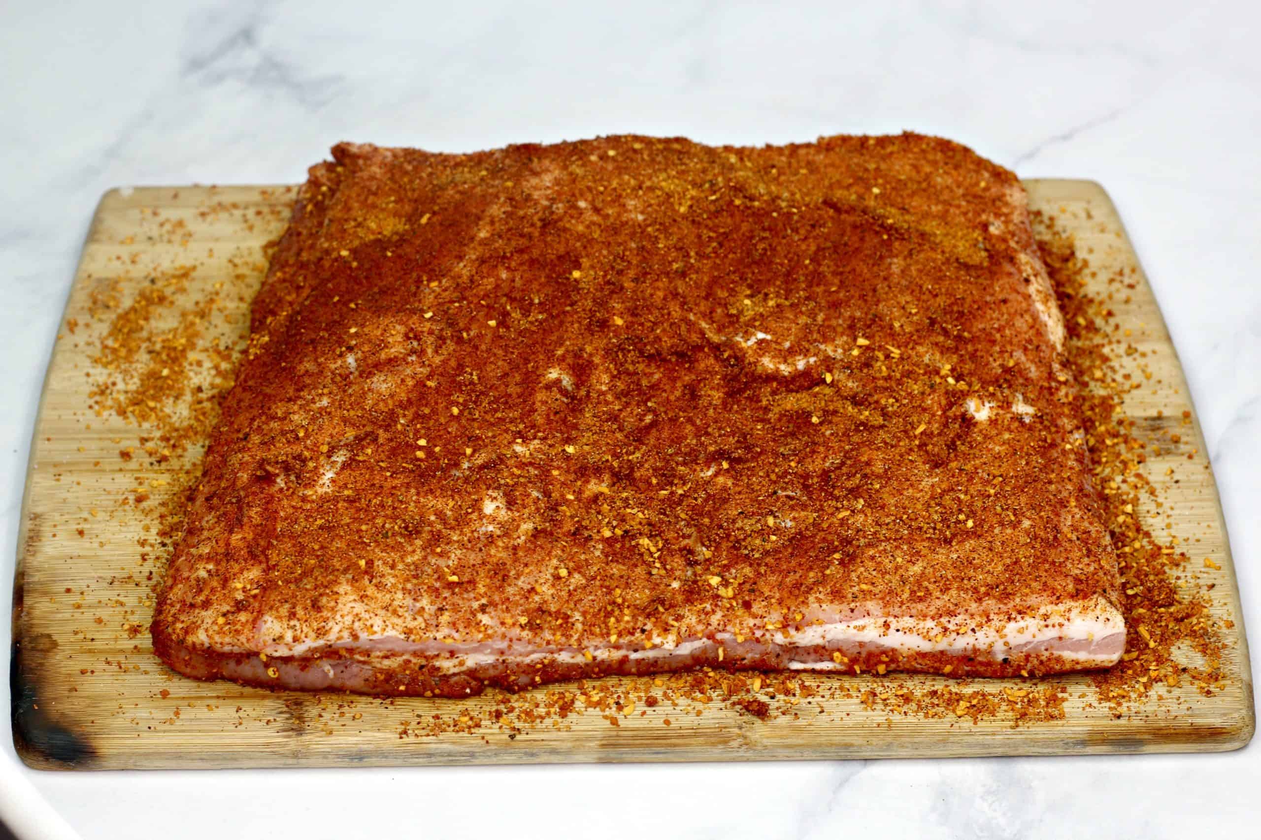 pork belly covered in dry rub on a wooden cutting board. 