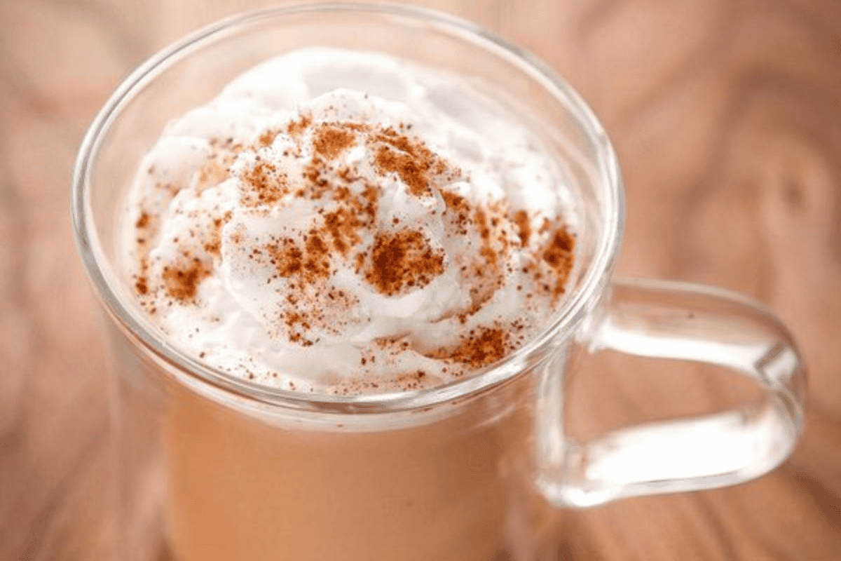 A chai tea latte in a clear glass mug topped with whipped cream and cinnamon.