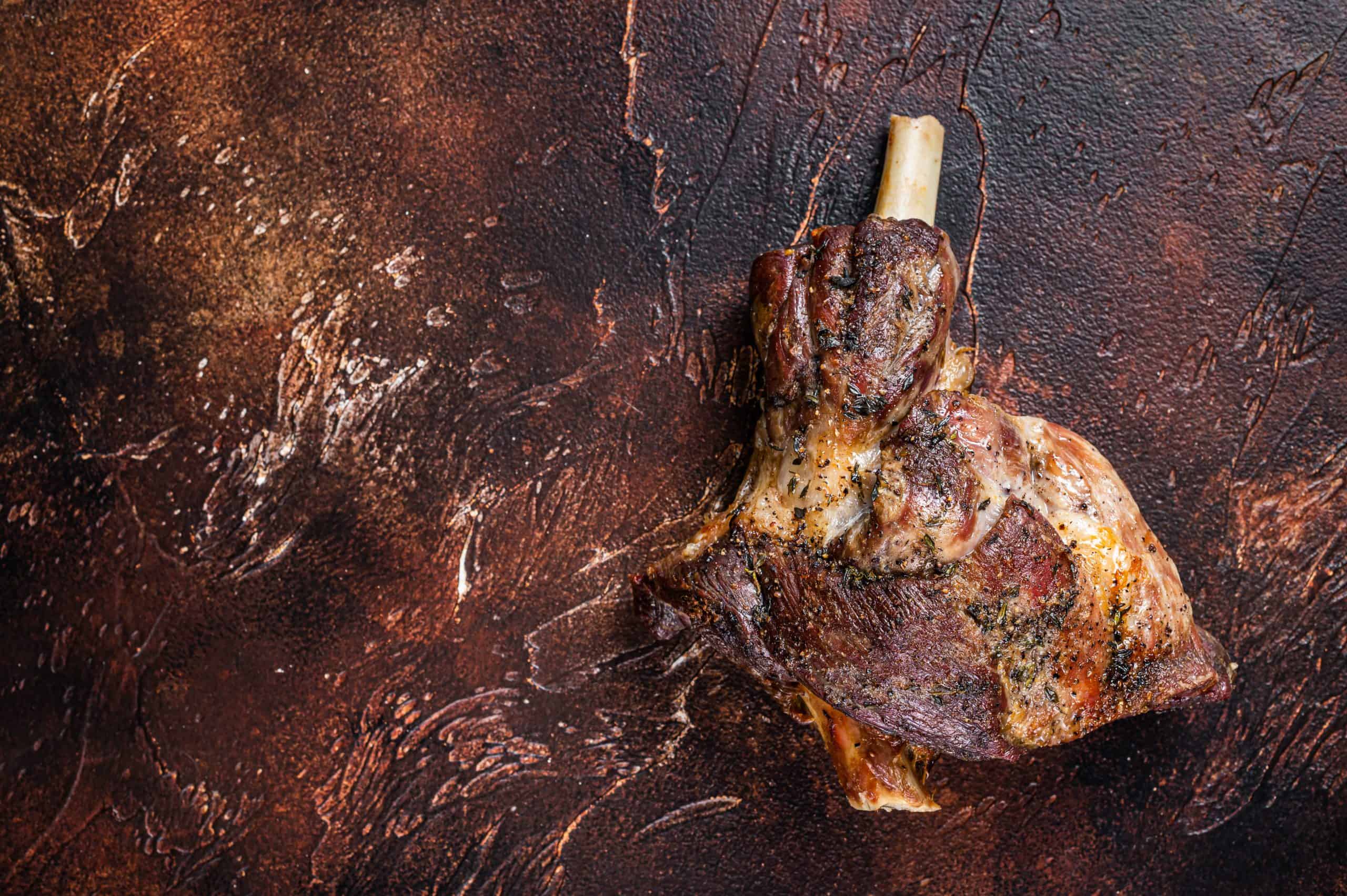 Roast Lamb leg with herbs and garlic. Dark background. Top view. Copy space.