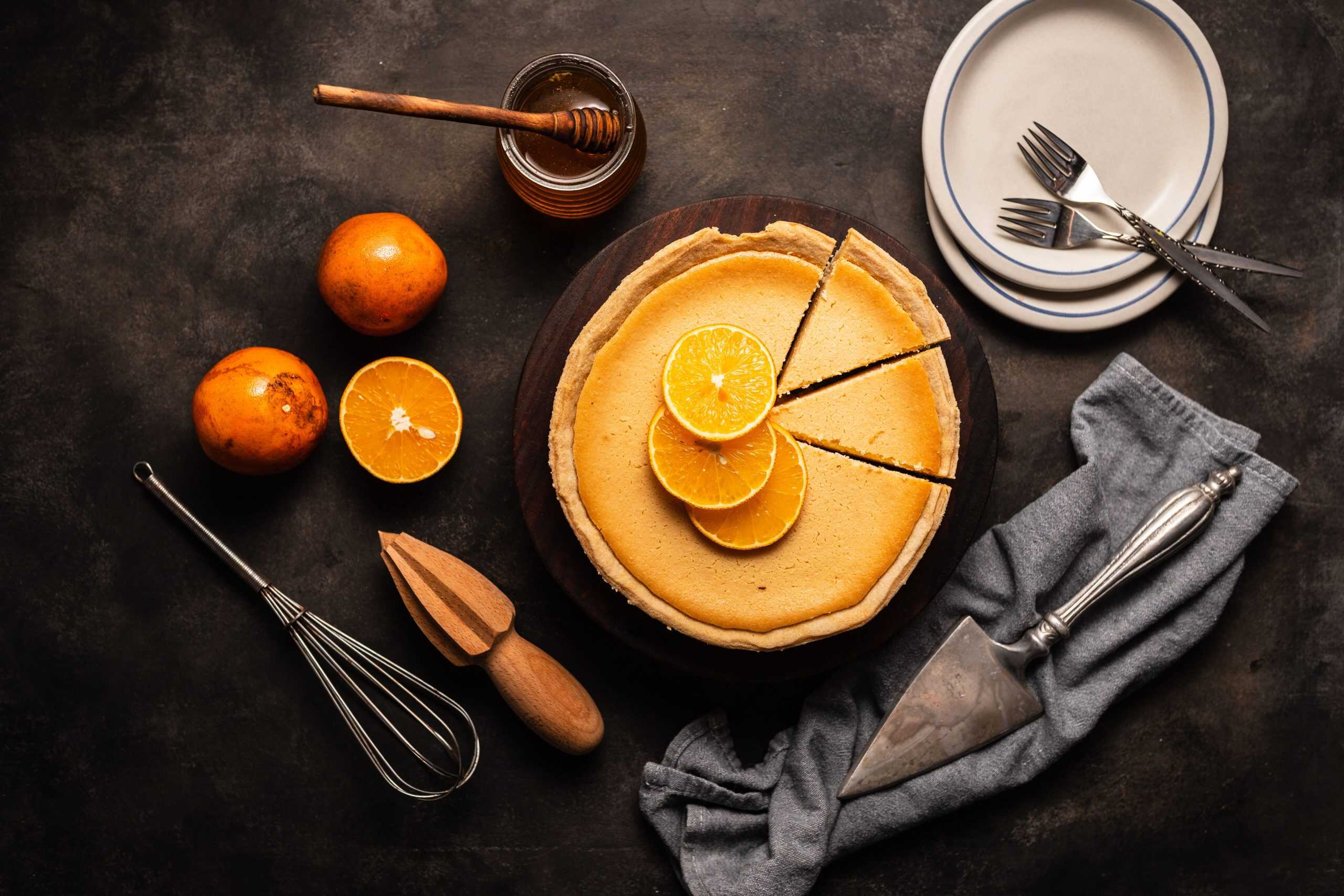 A top view of a homemade gourmet orange pie surrounded by cutlery and kitchen tools.