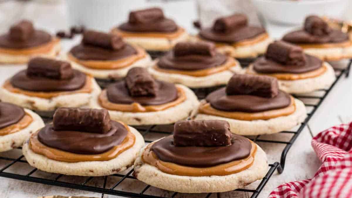 cookies on a cooling rack with caramel, chocolate and mini twix bars.
