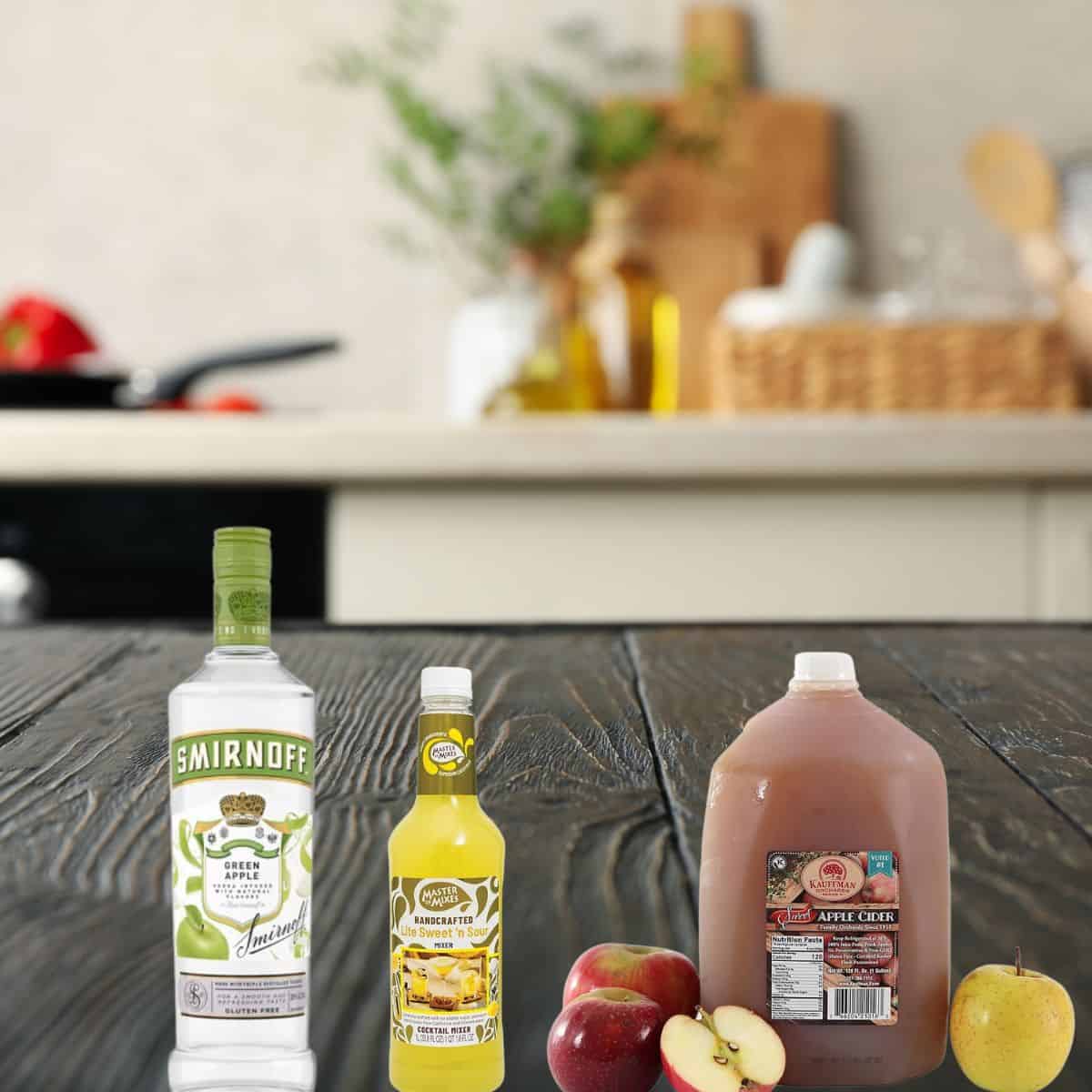 ingredients on a wooden counter including apple vodka, apple cider, sour mix and apples. 