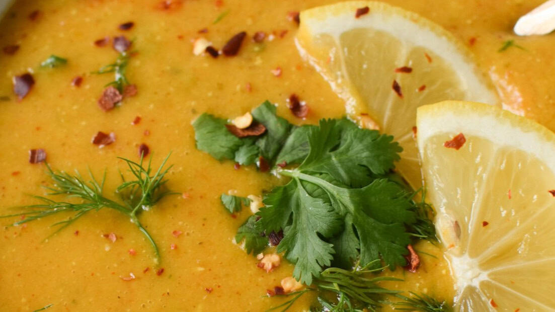 Bright yellow lentil soup with lemon slices and fresh herbs.