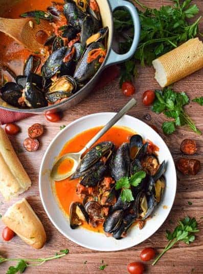 Bowl of chorizo tomato mussels with bread and parsley.