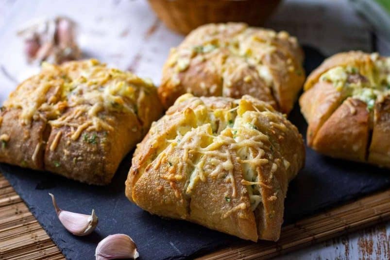 Four Korean cream cheese garlic bread rolls on a black slate.