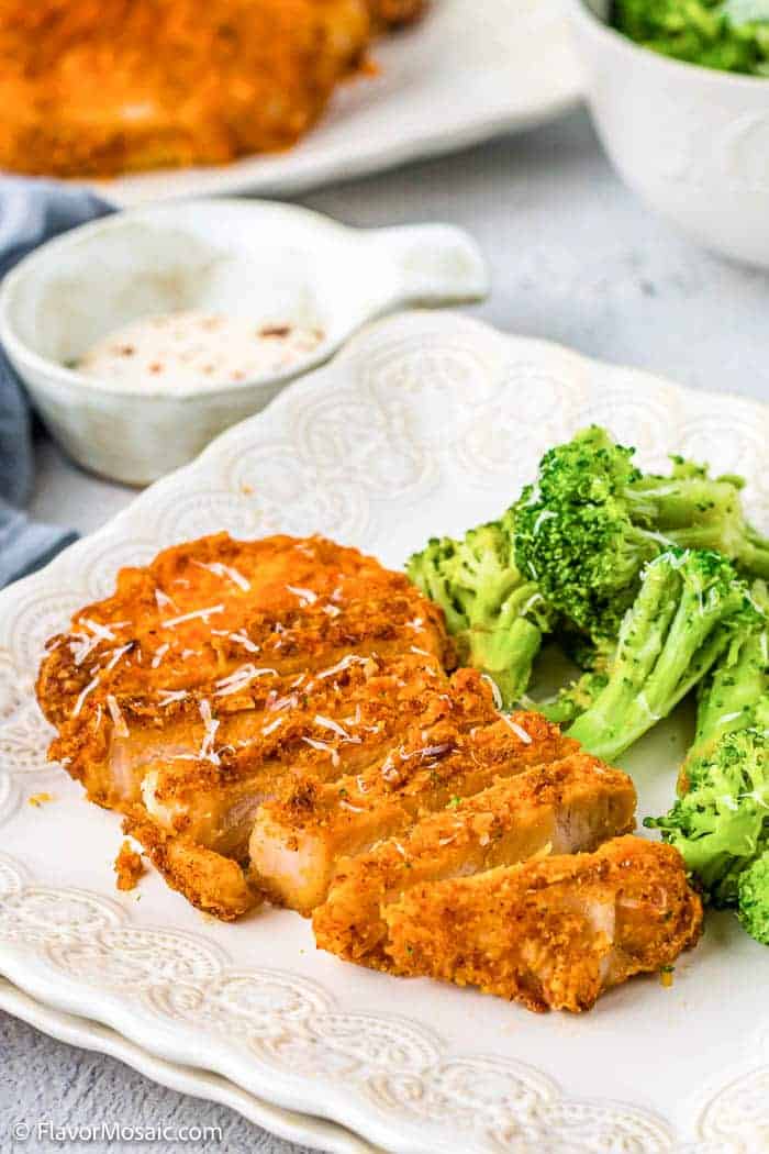 Overhead view of a pork chop sliced into strips sitting on a white plate next to cooked broccoli with shredded parmesan on top.
