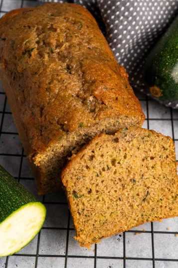 Zucchini bread on a cooling rack with a slice cut off.