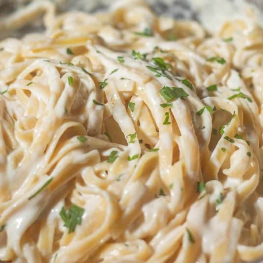 Creamy fettuccine pasta coated in cottage cheese Alfredo sauce, garnished with fresh parsley, shown up close with the rich sauce clinging to the pasta.