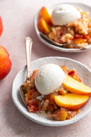 2 bowls of peach dump cake with vanilla ice cream and fresh peach.