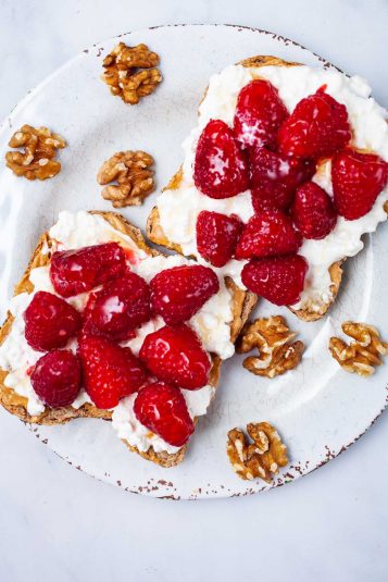 Two toasts on a plate with peanut butter, cottage cheese, fresh berries and a drizzle of honey.