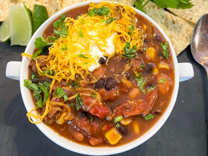 A serving of soup in a white bowl garnished with sour cream, shredded cheddar cheese, and diced cilantro.