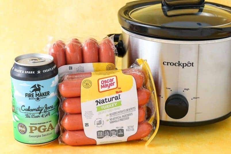 A plate of hot dogs served in a slow cooker with onions and mustard.