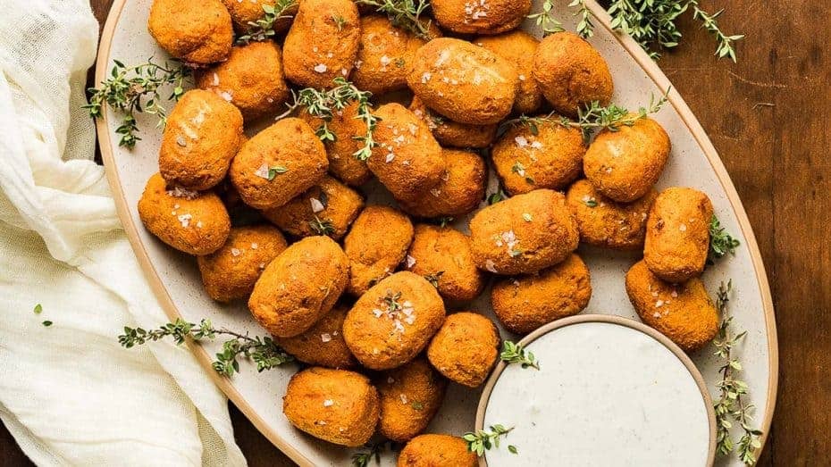 A plate full of sweet potato tater tots with dip.