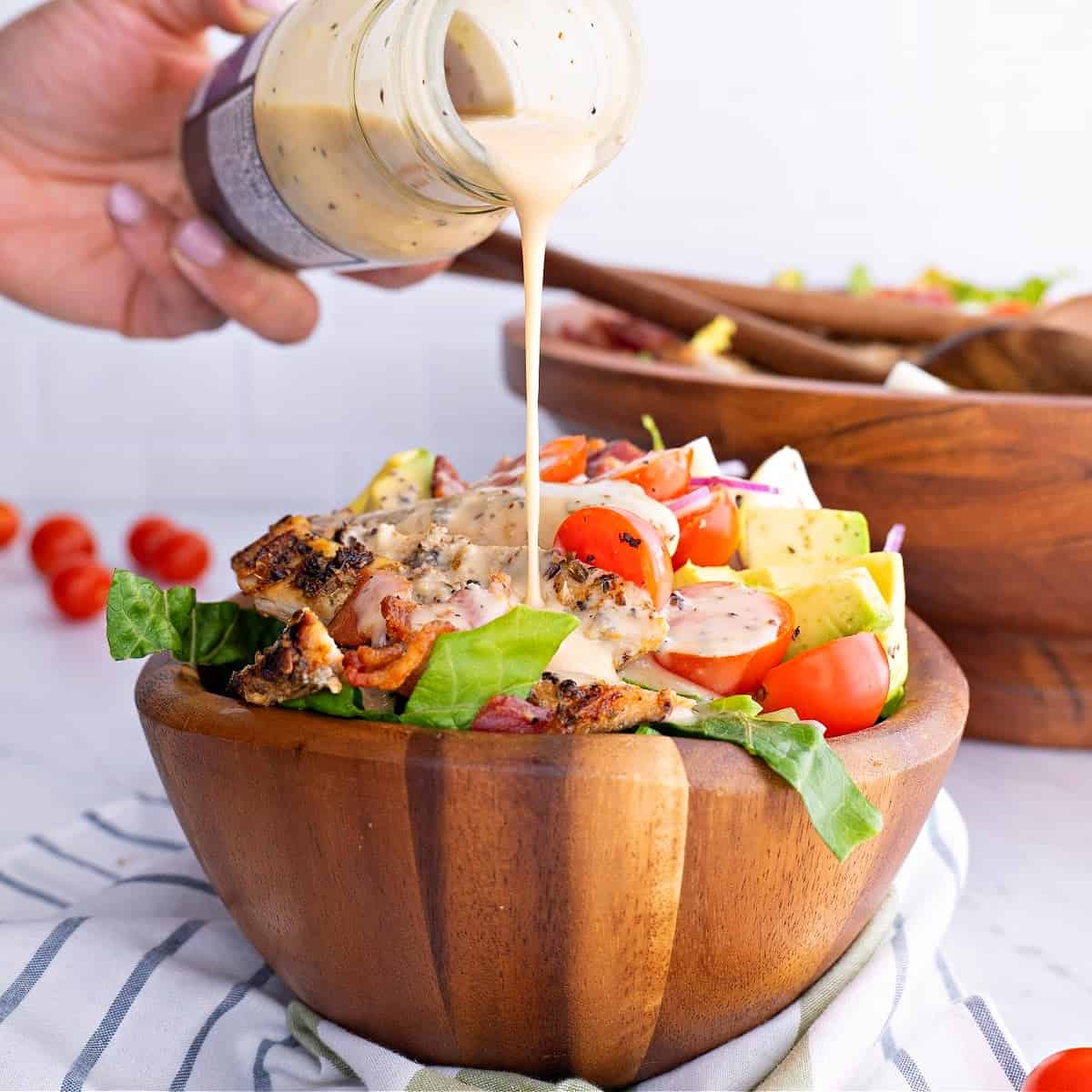 A photo of Chicken Cobb Salad in a bowl with dressing being poured on top.