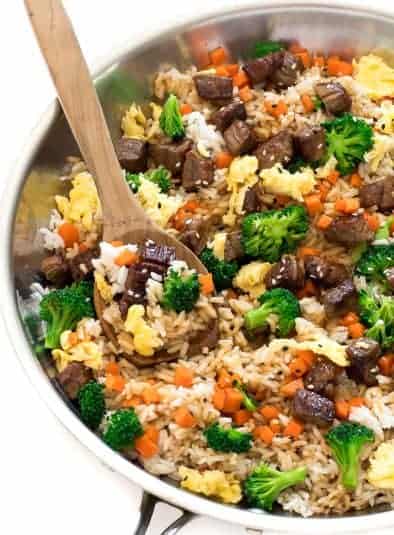 Beef fried rice in skillet with wooden spoon.