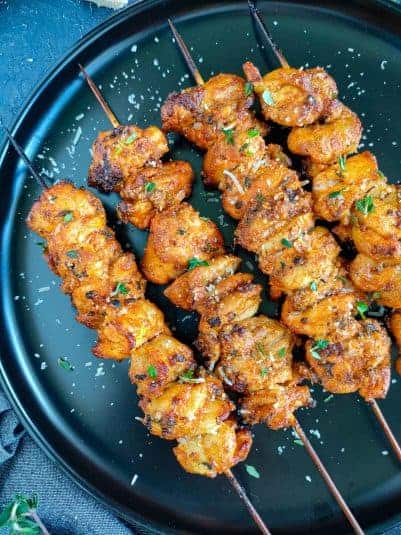 Lemon garlic parmesan chicken skewers on a black plate.