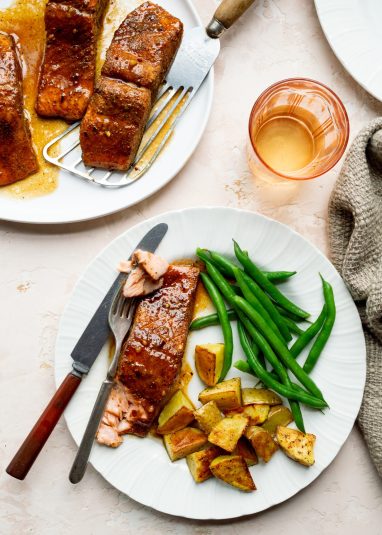 White plate of Honey Butter Old Bay Salmon with green beans and roasted potatoes.