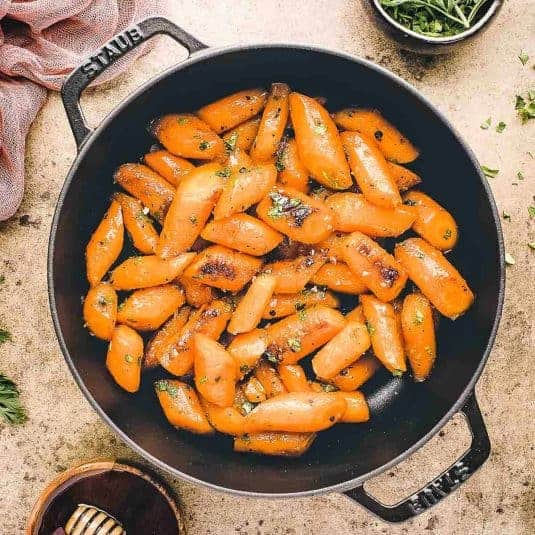 Overhead view of three servings of vanilla creme brulee on white plates and napkins with a blue background.