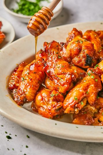 Hot honey chicken wings on a platter with honey being drizzled on top.
