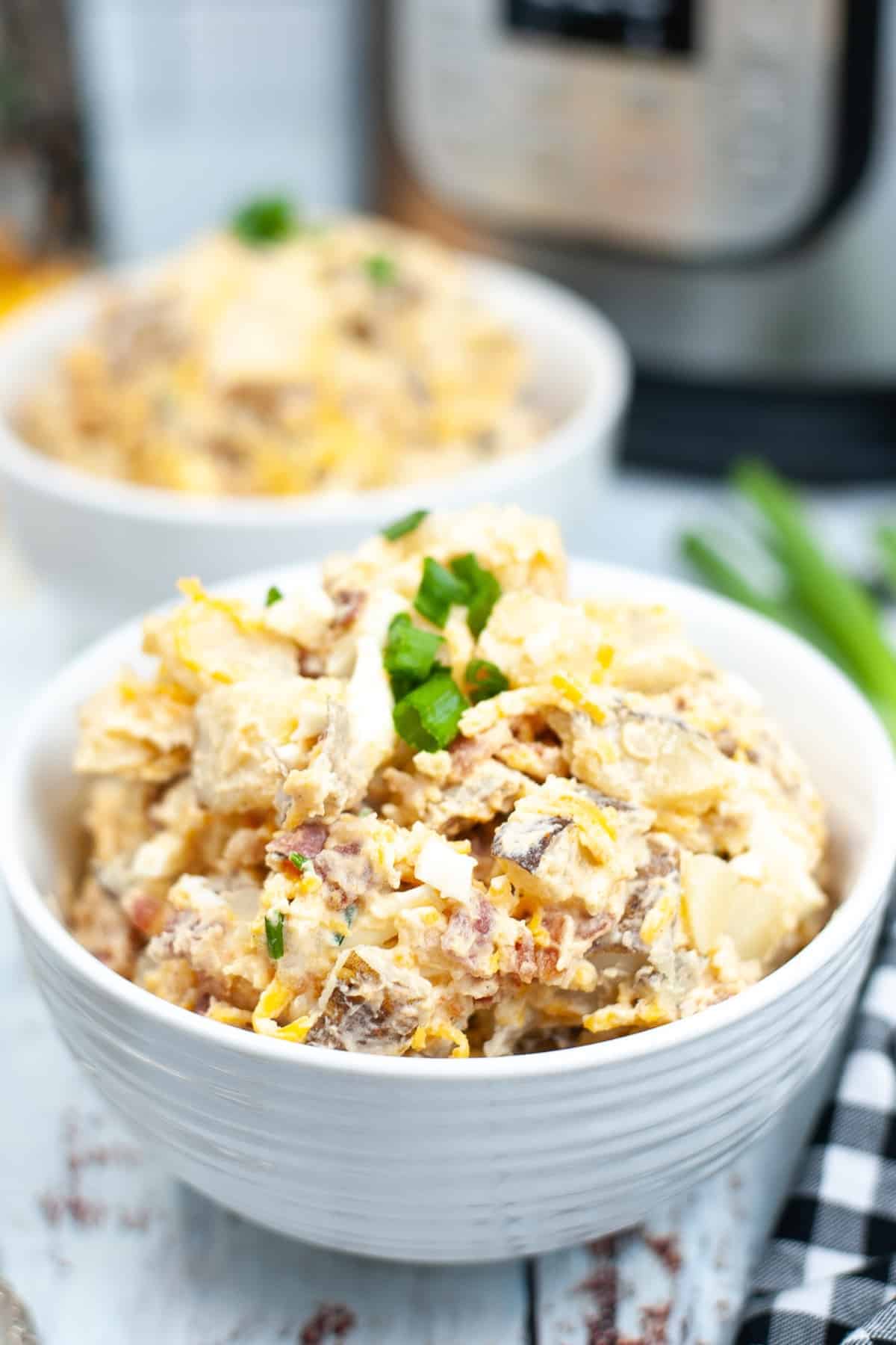 Two white bowls of potato salad topped with chopped green onions.