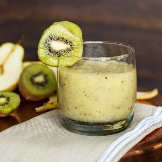 Two champagne pomegranate cocktails in coupe glasses on a dark blue background scattered with pomegranate seeds.