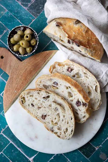 Freshly baked No-Knead Olive Bread with a golden, crispy crust and chunks of kalamata and green olives visible throughout.