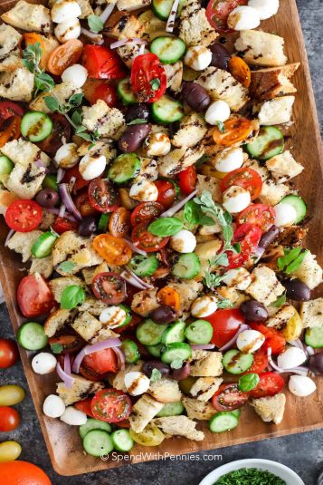 A panzanella salad on a wood board with herbs.