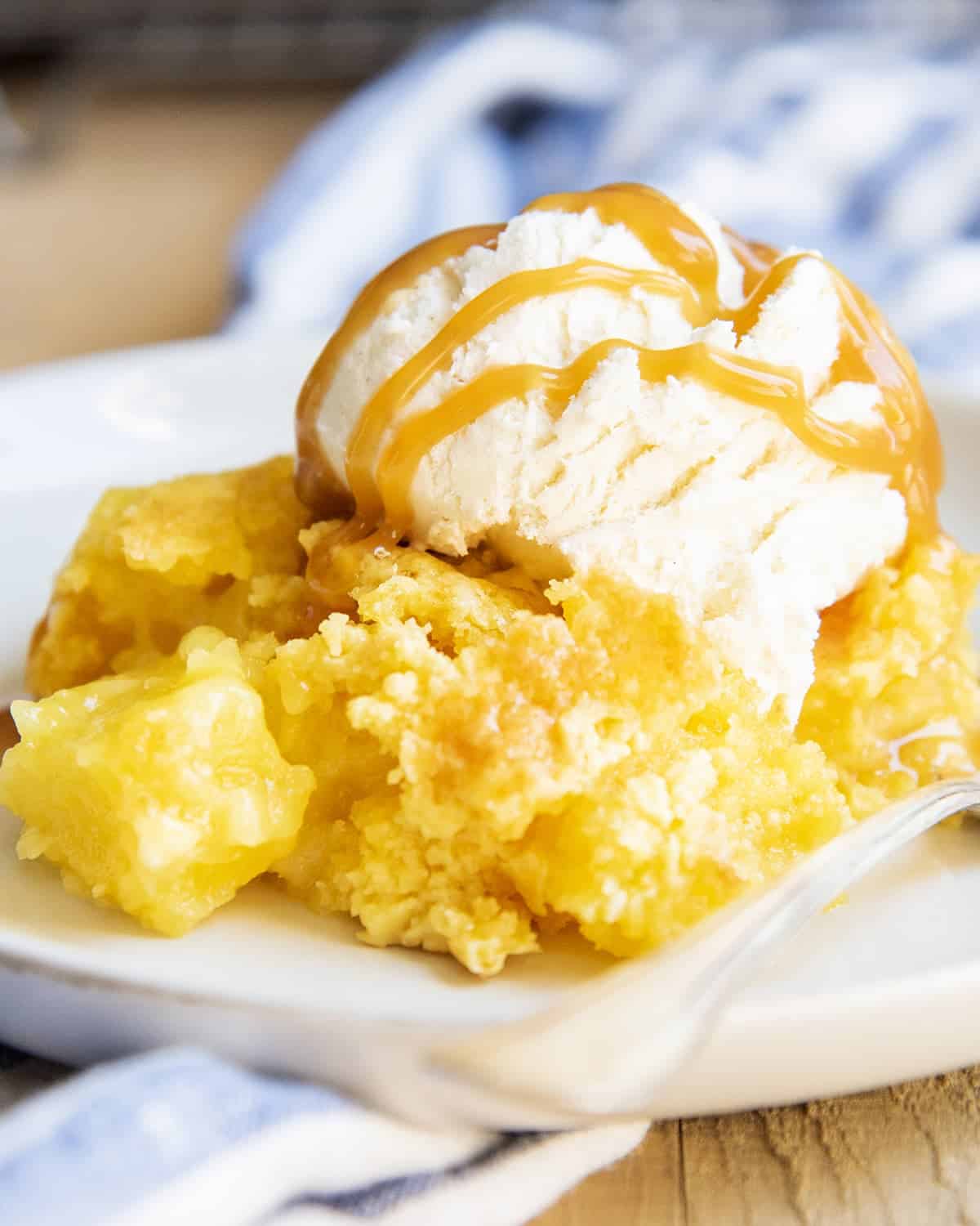 A serving of pineapple cobbler on a plate topped with vanilla ice cream and caramel syrup.