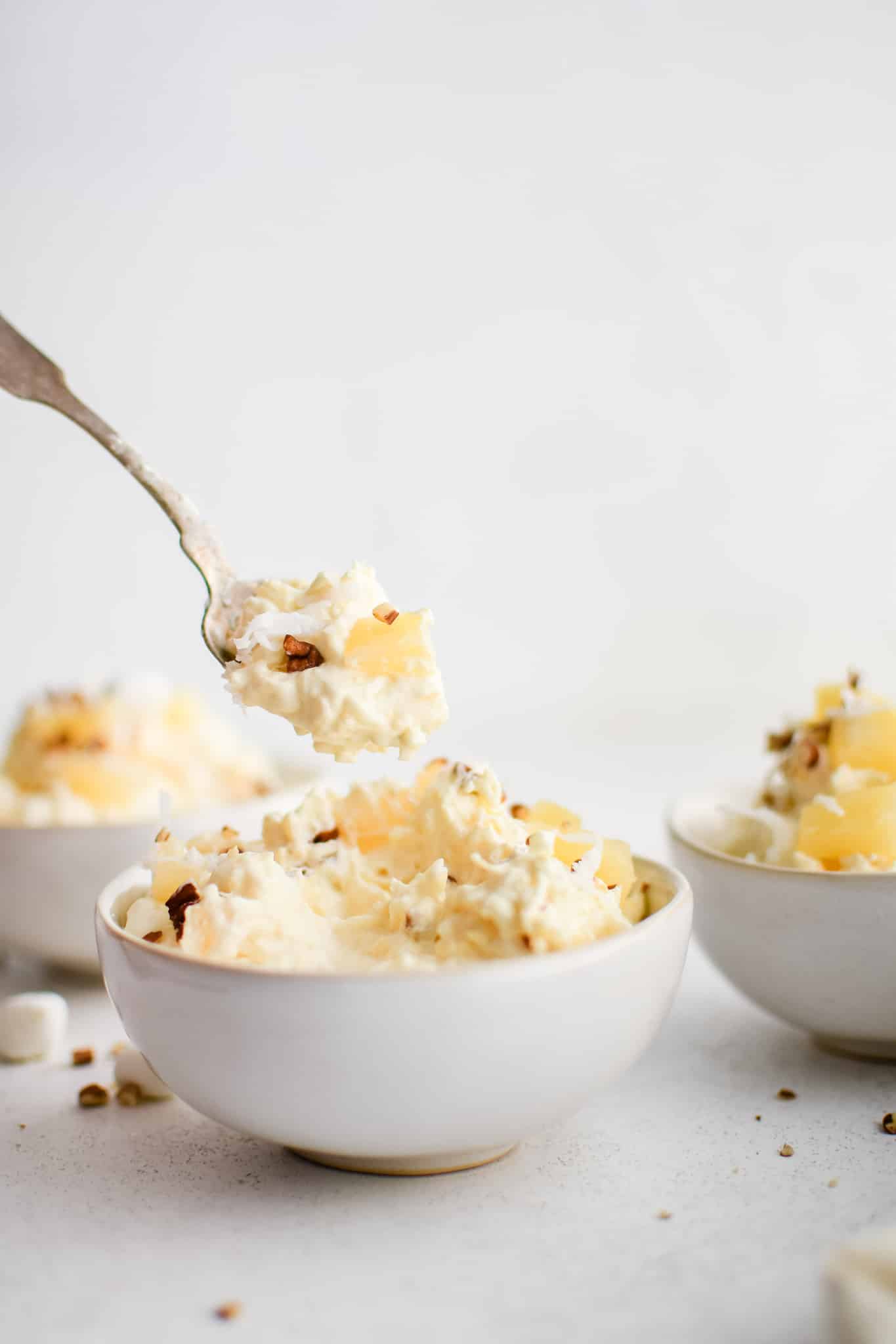 Large white serving bowl filled with prepared creamy pineapple fluff dessert topped with pineapple chunks, mini marshmallows, and chopped pecans.