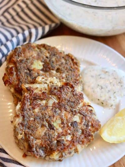2 sardine fish cakes on a plate with yogurt dill sauce.